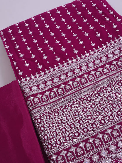 A close-up of a magenta pink fabric with intricate silver mirror work embroidery, showing detailed patterns and borders.