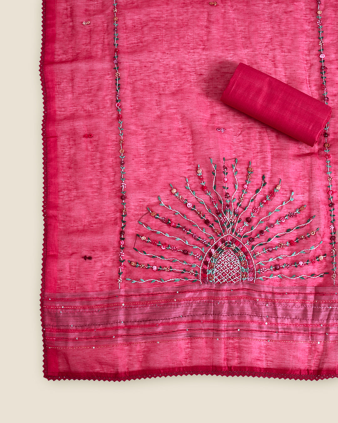 A bright pink silk saree fabric with a matching rolled-up pallu, featuring a detailed silver and red sequin peacock motif and a scalloped border on a light beige background.