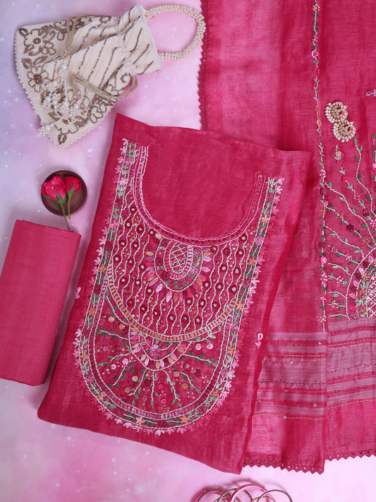 A pink traditional embroidered fabric set laid flat on a pink background, including a heavily embellished embroidered panel, matching fabric pieces, a small floral accessory, and a decorative mask.
