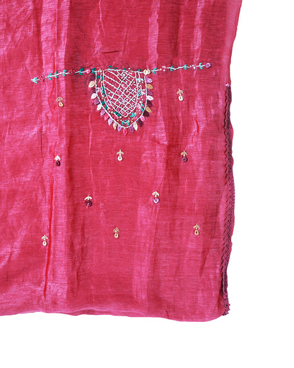A close-up of a pink fabric garment or textile with embroidered detailing, including a central decorative motif and small metallic embellishments, shown against a white background.