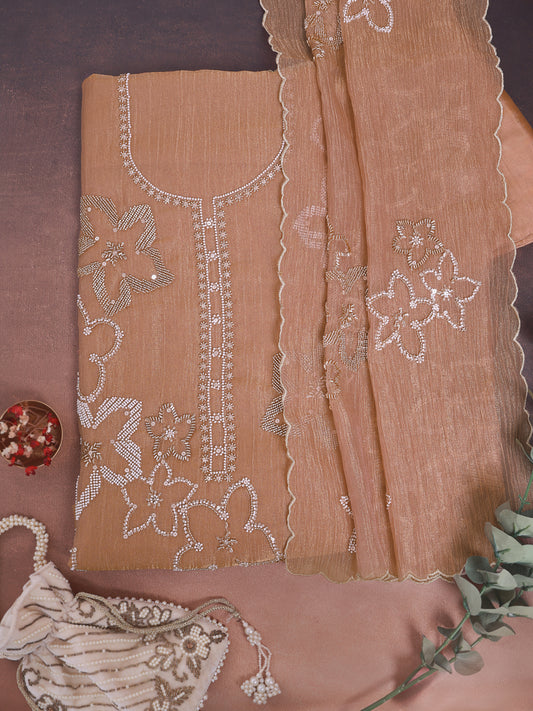 A peach-beige embroidered ethnic suit material set with a matching dupatta, laid flat on a mauve background. The fabric features white and metallic silver floral embroidery and beadwork.