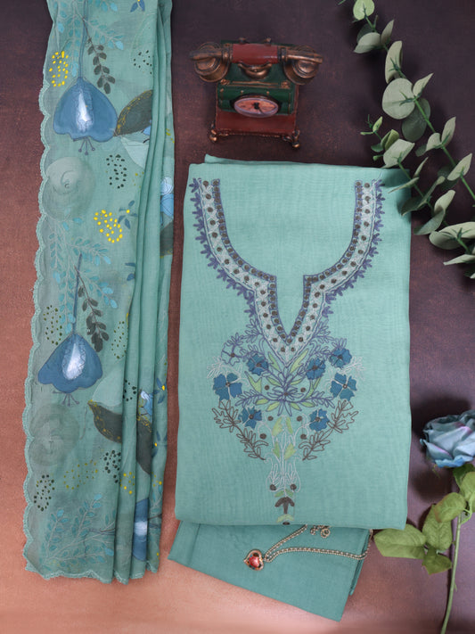 A folded mint green salwar suit set with floral embroidery, featuring a matching printed dupatta and decorative accessories, arranged on a brown surface.