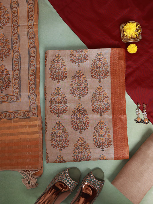 A folded beige and rust-orange block-printed cotton saree fabric with a matching border, styled in a flat-lay arrangement with a red dupatta, metallic shoes, and yellow flower petals on a mint green background.