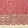 Pink fabric with intricate gold embroidery and scalloped edge on a beige background