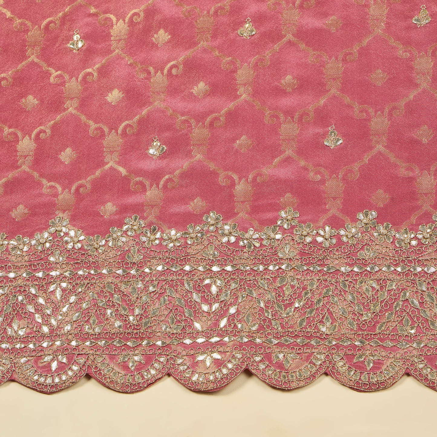 Pink fabric with intricate gold embroidery and scalloped edge on a beige background