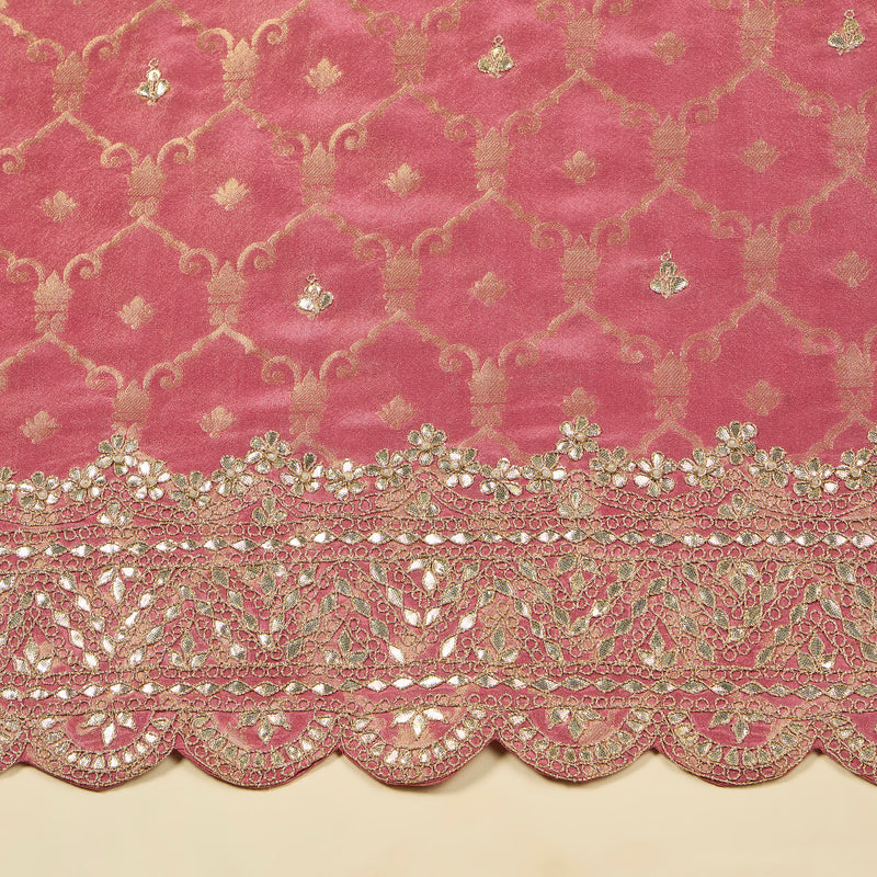 Pink fabric with intricate gold embroidery and scalloped edge on a beige background